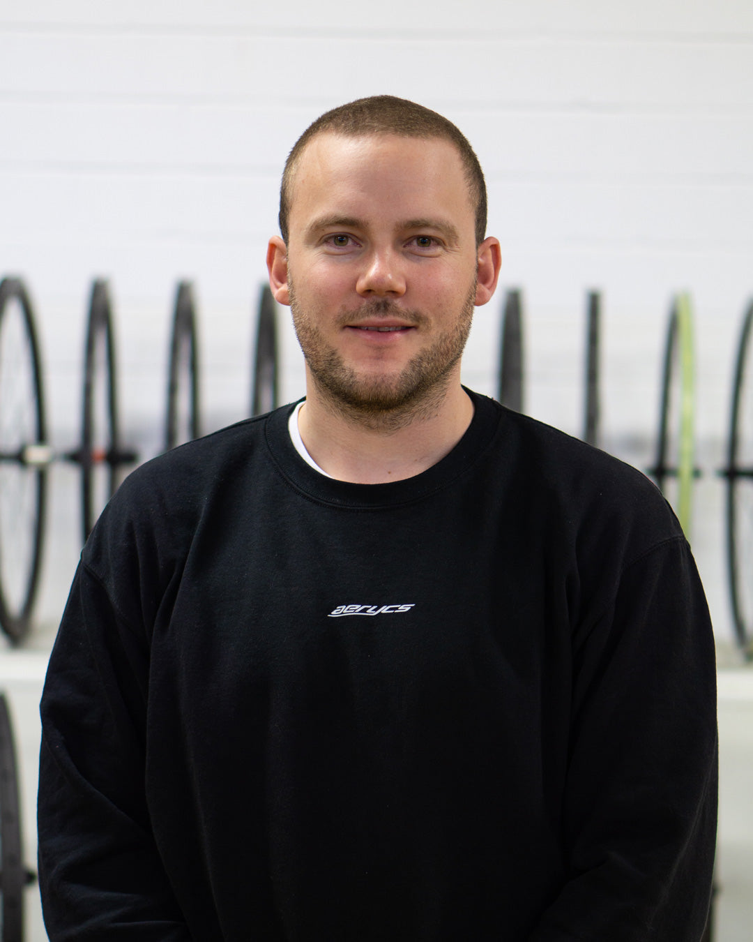 Mark with an aerycs sweatshirt with a white wall and bicycle tyres in the background